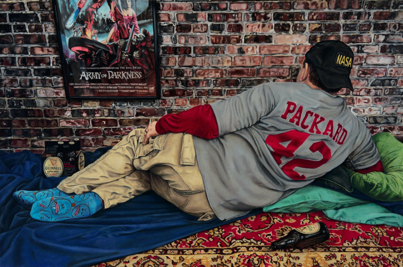 Brodalisque Reclining in the Basement is staged in a basement with a brick wall with a red and gold rug plus a framed Army of Darkness poster. The bro, dressed in a gray sports-shirt with red letters and numbers, faces away from the viewer. 