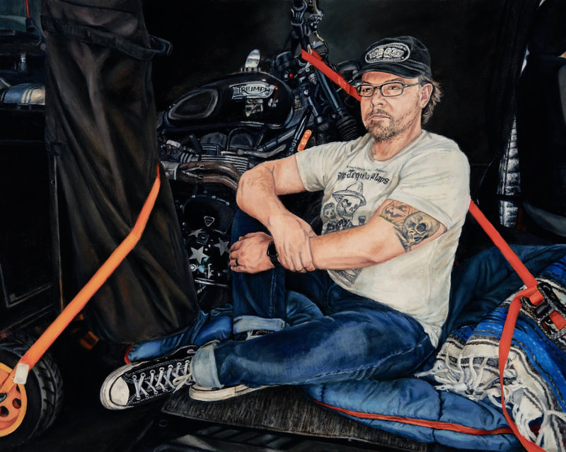 Brodalisque Seated in the Transit shows a scruffy dude inside of a van surround by motorcycle gear held in place with orange ratchet straps. The man wears a white white t-shirt and blue jeans. 