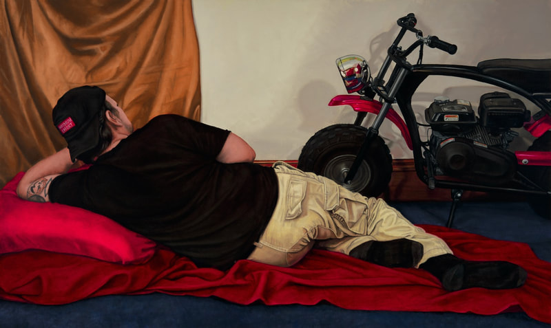 Brodalisque with Cargo Pockets includes a model wearing a black t-shirt; he faces away from the viewers to show off his beige cargo pants. He lounges on red drapery, which echoes the red accents on the minibike in the background. 