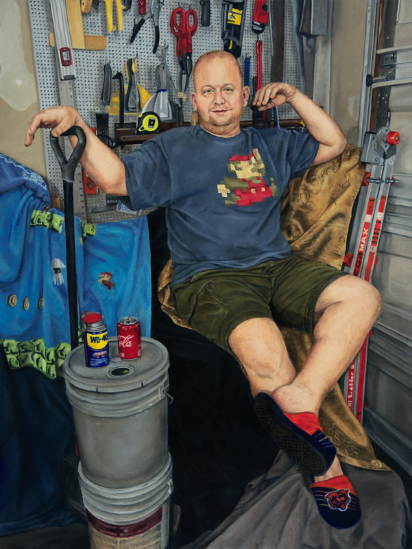 Man Cave Boy shows a slipper-clad man sitting on cushions and drapery in a garage in front of a pegboard workbench. His right hand rests on a shovel handle, and his left foot is crossed over his right leg as he smiles at the viewers. 